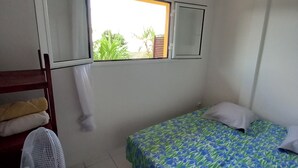 A small, clean room with a bed, a fan, a window, and a mirror.