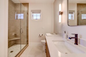 Un baño moderno con ducha envuelta en vidrio, inodoro blanco y tocador con lavamanos y espejo.