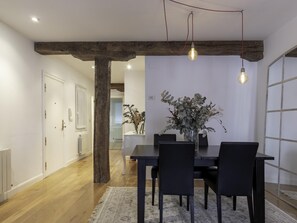 A dining area with a wooden beam ceiling, a table with chairs, and a vase with dried flowers.