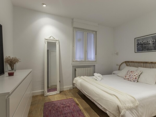A bedroom with a bed, a dresser, a mirror, a window with curtains, and a framed picture on the wall.