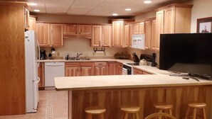 Una cocina con armarios de madera, una isla central con taburetes, un refrigerador y un microondas.