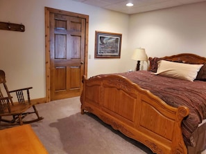 Ein Schlafzimmer mit einem hölzernen Bett, einem Schaukelstuhl, einer Tür und einem gerahmten Bild an der Wand.