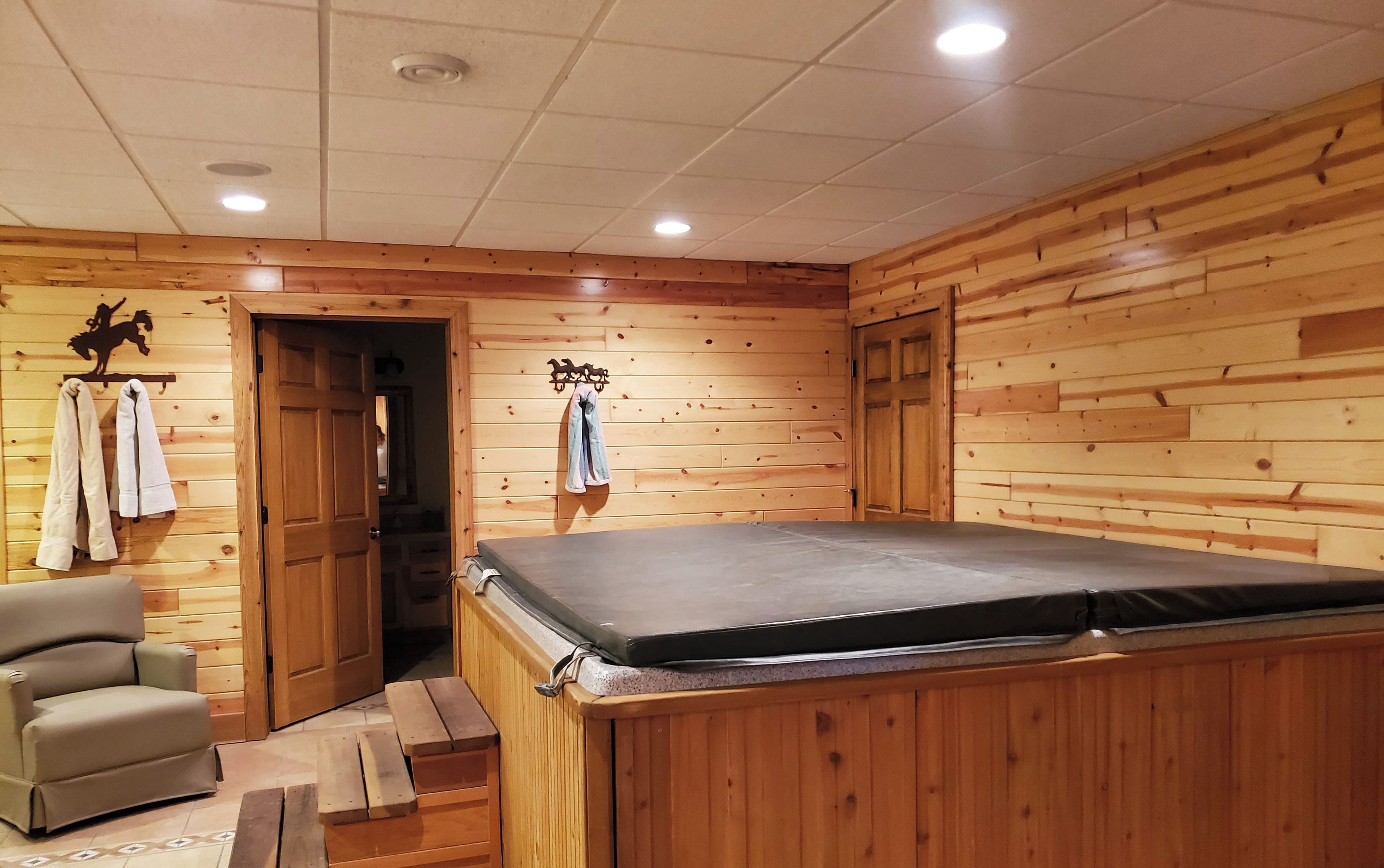 Una habitación de madera con una camilla de masaje, una silla y una puerta que da a otra estancia.