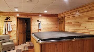 Una habitación de madera con una camilla de masaje, una silla y una puerta que da a otra estancia.