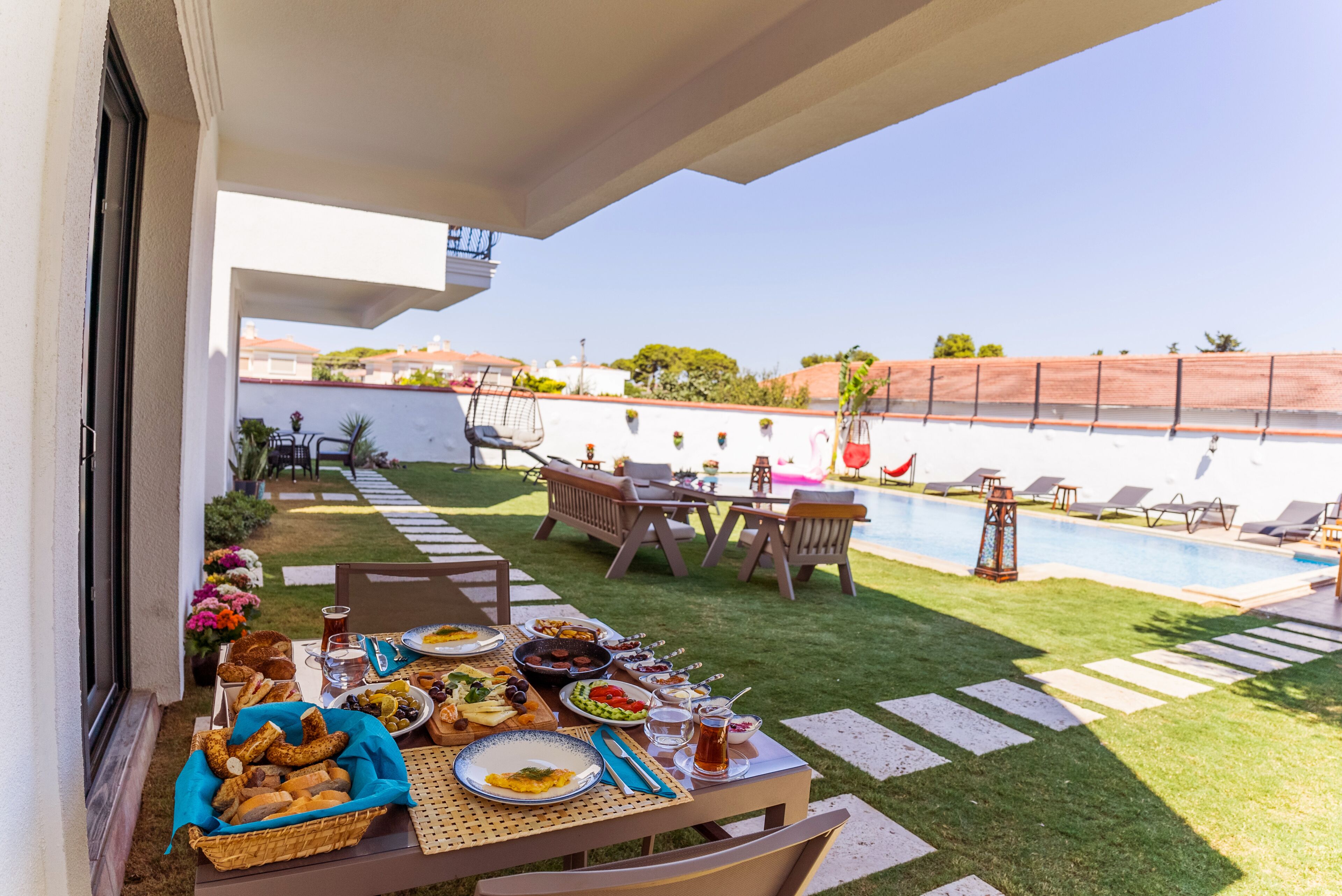 An outdoor dining area with a table set for a meal, surrounded by chairs and a pool.