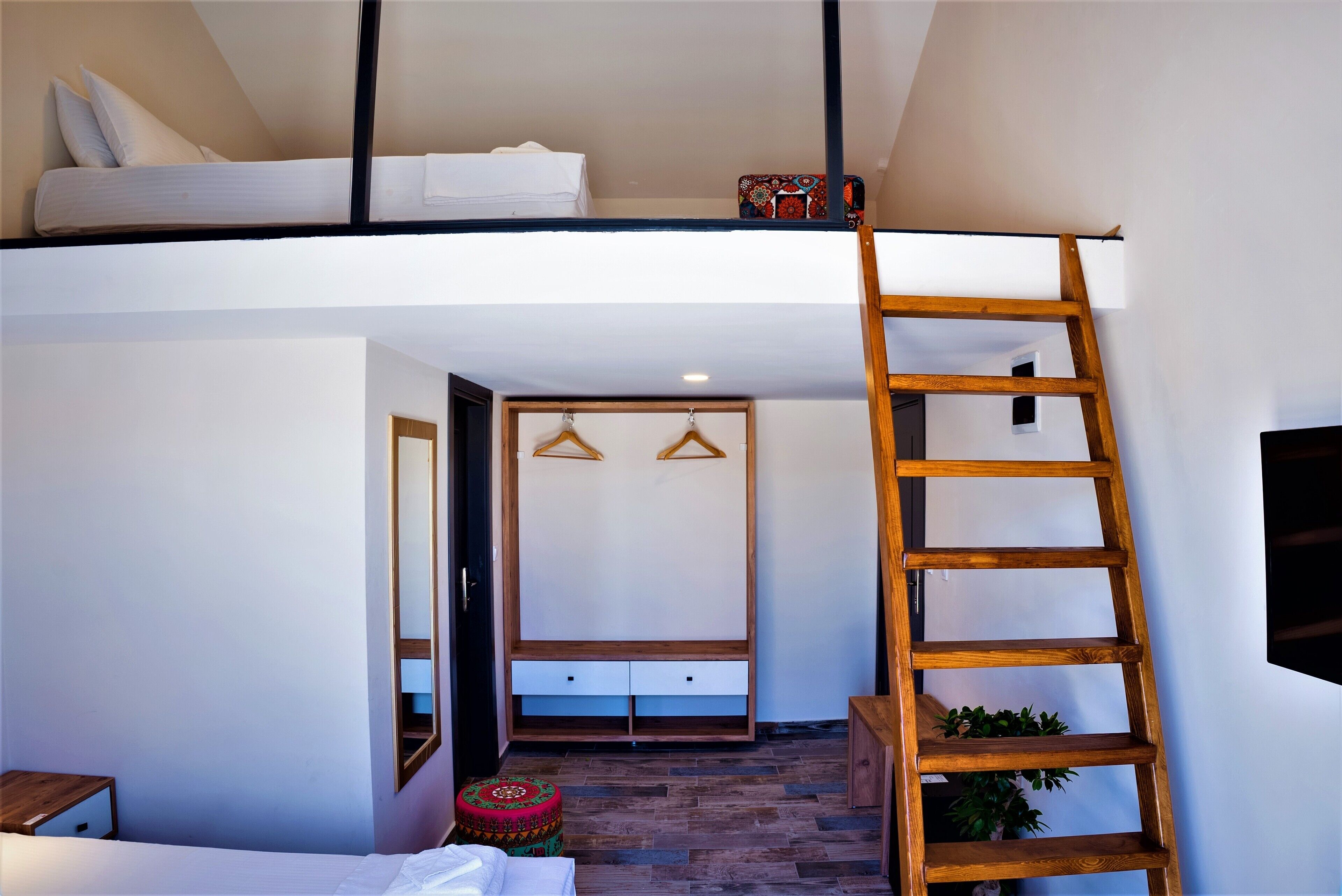 A loft bedroom with a bunk bed, a wooden ladder, a wardrobe, and a small stool.