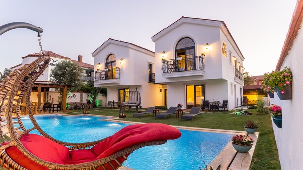 Un área junto a la piscina con una silla de mimbre, una piscina y un edificio de dos plantas con balcones.