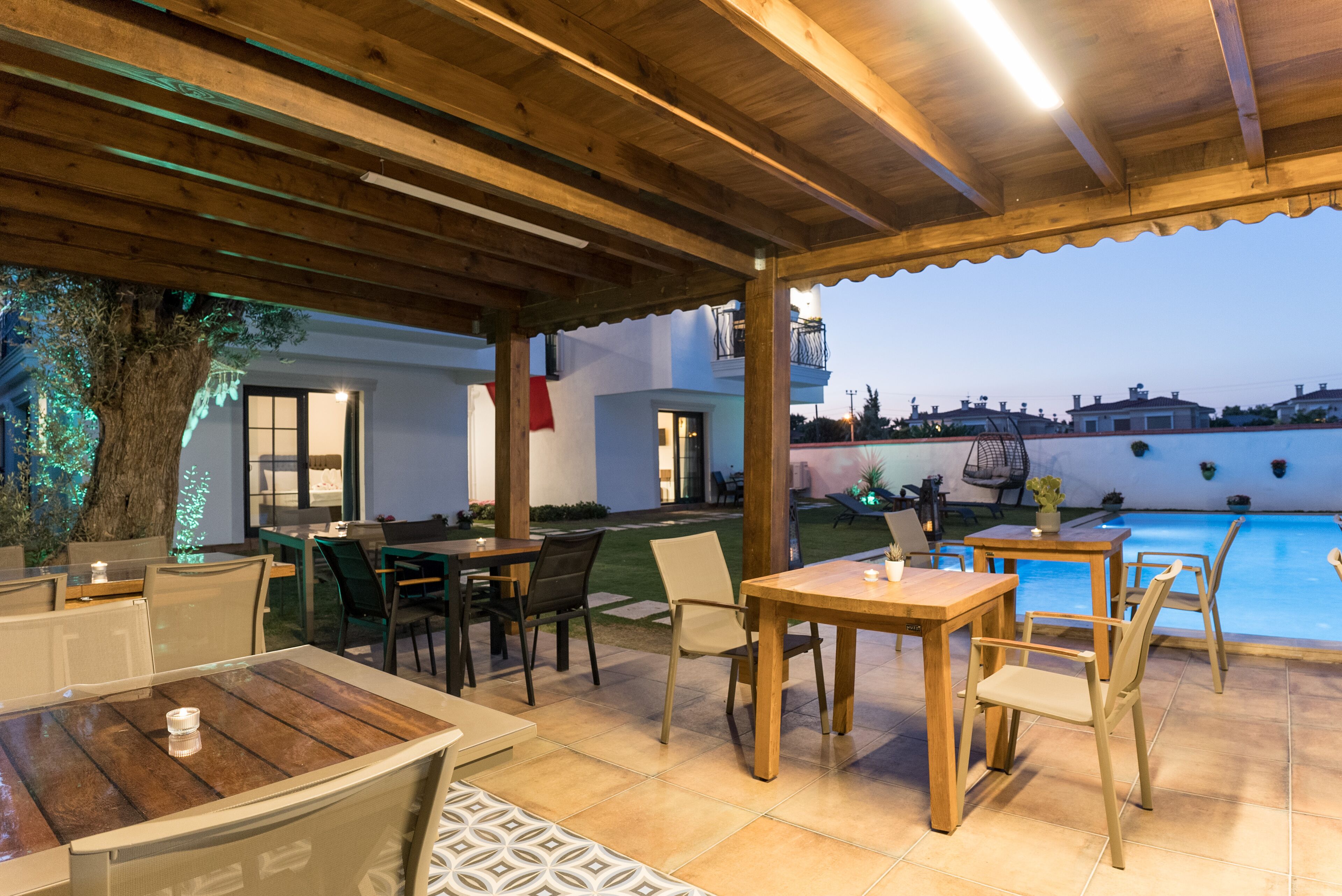 Un'area patio esterna con tavoli e sedie in legno, una piscina e vista sul quartiere circostante.