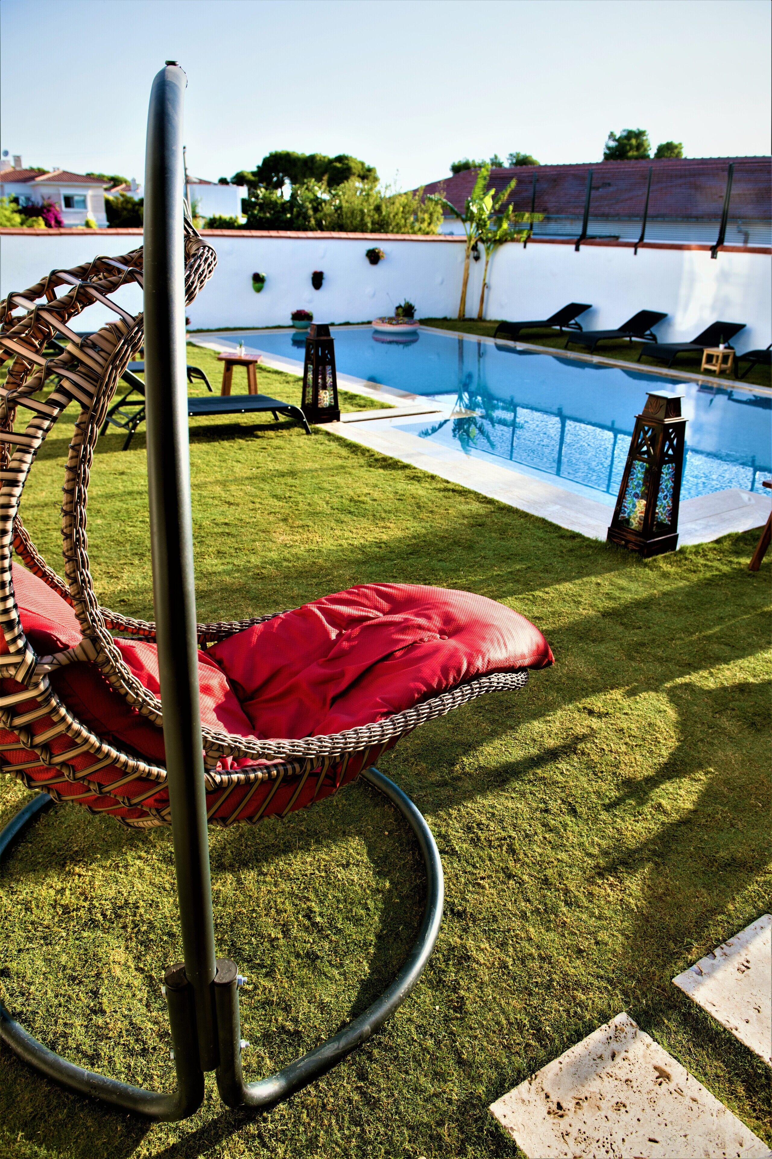A wicker chair with a red cushion, a pool, and a white wall with a fence in the background.