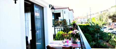 A balcony with a table and chairs, a potted plant, and a view of a residential area.
