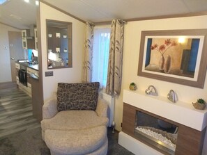 Ein Wohnzimmer mit Kamin, einer Couch, einem Spiegel und einer Küchenzeile im Hintergrund.