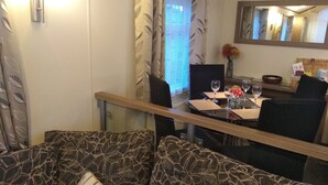 Ruokailutila, jossa on kahdelle katettu pöytä, kuviollisilla koristetyynyillä varustettu sohva ja seinällä peili.