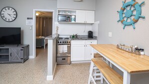 A compact kitchen with white cabinetry, a microwave, a stove, and a wooden dining table with benches. - Anchors UP #3; WALK to Beach/Bars/Dining (Clearwater Beach)