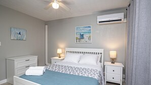 A bedroom with a bed, two bedside tables with lamps, a ceiling fan, an air conditioning unit, and two wall-mounted paintings. - Anchors UP #3; WALK to Beach/Bars/Dining (Clearwater Beach)