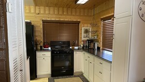 A kitchen with wooden panel walls, a black stove, white cabinets, and a patterned rug. - Cozy cabin in Duck Creek (Duck Creek Village)