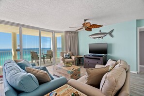 A balcony with a view of the ocean, a ceiling fan, a fish decoration, a television, and a seating area with a coffee table.