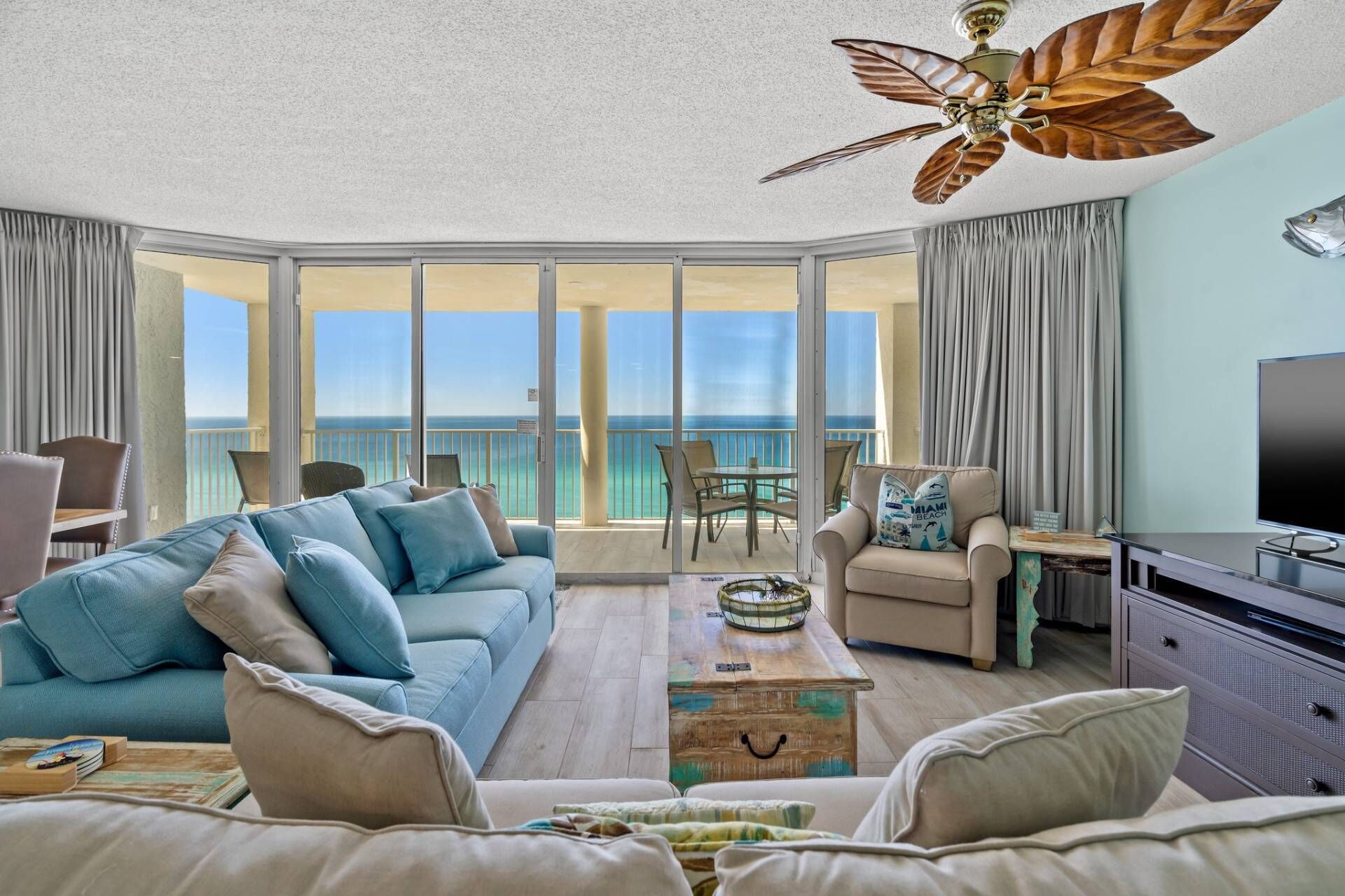 Een ruime woonkamer met een grote bank, een salontafel en een televisie. Er is een balkon met uitzicht op de oceaan.
