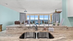 A modern kitchen with a double sink, a dining area with a view of the ocean, and a ceiling fan. - Long Beach Resort Tower 1 Unit 1303 (Panama City Beach)