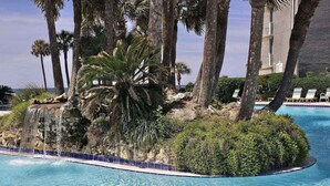 A pool surrounded by palm trees and a rocky island. - Long Beach Resort Tower 1 Unit 1303 (Panama City Beach)