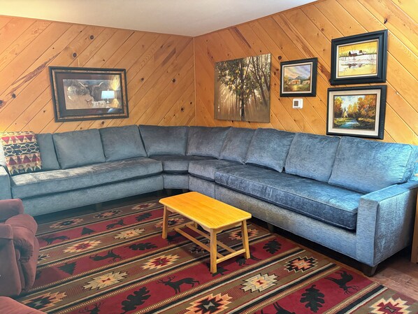 A corner living room with a gray sectional sofa, a wooden coffee table, and a patterned rug.