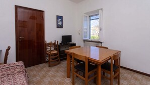 Een kamer met een houten deur, een televisie, een eettafel met stoelen, een vloer met patroon en een raam met uitzicht.
