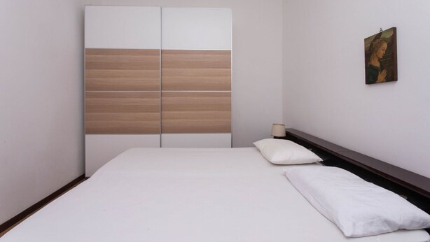 Een slaapkamer met een bed, nachtkastje, lamp en een garderobe met horizontale strepen.