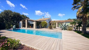 Une maison moderne dotée d’une piscine, entourée d’une terrasse en bois et agrémentée de diverses plantes.