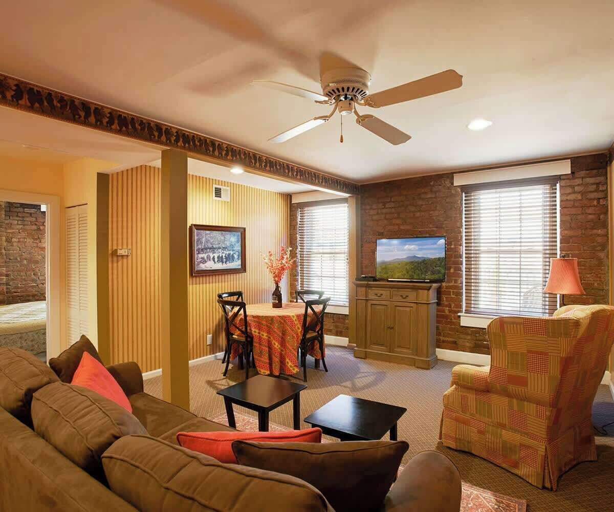 A living room with a sofa, a dining table with chairs, a television, and a ceiling fan.