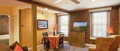 A living room with a sofa, a dining table with chairs, a television, and a ceiling fan.