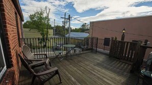 Une terrasse en bois avec des meubles d’extérieur, un mur de briques et une vue sur un immeuble et des arbres.