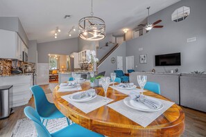 A modern dining area with a round wooden table set for six, blue chairs, and a contemporary chandelier.