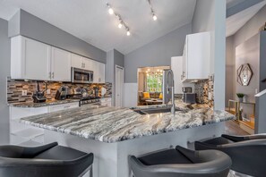 A modern kitchen with a large island, white cabinets, and a stone backsplash.