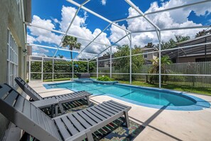 A covered outdoor swimming pool with lounge chairs and a patterned rug.