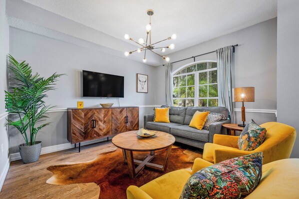 A modern living room with a sofa, armchairs, a coffee table, a TV, and a large window with curtains.