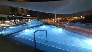 A rooftop pool area with clear blue water, a metal railing, and a view of the city at night. - Dubai Dream - Hotel Suite - Breathtaking view of Palm Jumeira +++ (Dubai)