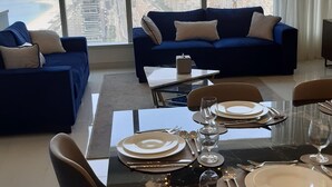 A modern living room with a dining area, large windows with a city view, and a high ceiling with a unique light fixture. - Dubai Dream - Hotel Suite - Breathtaking view of Palm Jumeira +++ (Dubai)