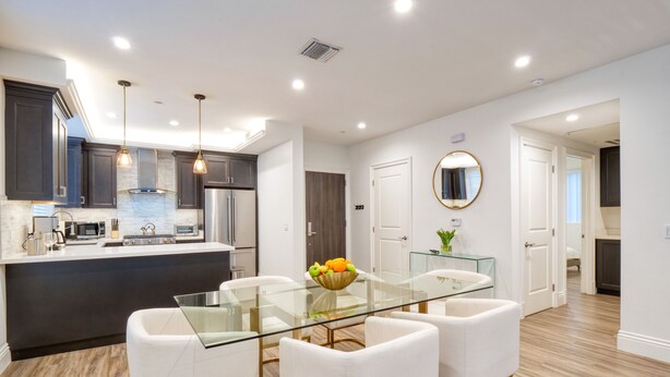 A modern kitchen with dark cabinets, stainless steel appliances, and a glass dining table with white chairs.