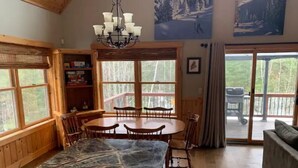 A spacious dining area with a marble table and chairs, wooden walls, and large windows offering a view of the outdoors. - 4bdrm Chalet-close to downtown & outdoor adventure (Bethel)