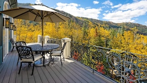 A wooden deck with a round table and chairs, an umbrella, and a view of autumn foliage and mountains. - Exquisite pet friendly home, 5 blks from Gondola with stunning views!! (Aspen)