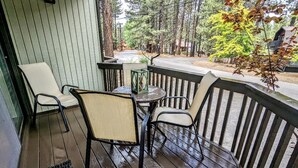 A wooden porch with two chairs and a table, overlooking a road and trees.