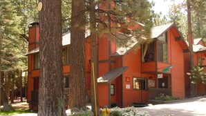 A red lodge with a stone foundation, surrounded by trees and a flower bed.