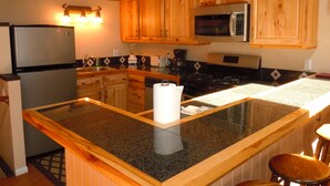 Una cocina con gabinetes de madera, un refrigerador, un microondas, una estufa y una encimera de granito.