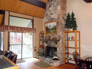 A cozy living room with a stone fireplace, wooden shelves, and a dining area with a table and chairs.