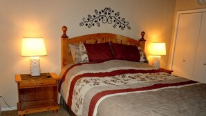Una cama bien tendida con una colcha estampada con motivos florales, dos lámparas de noche y un adorno en la pared.