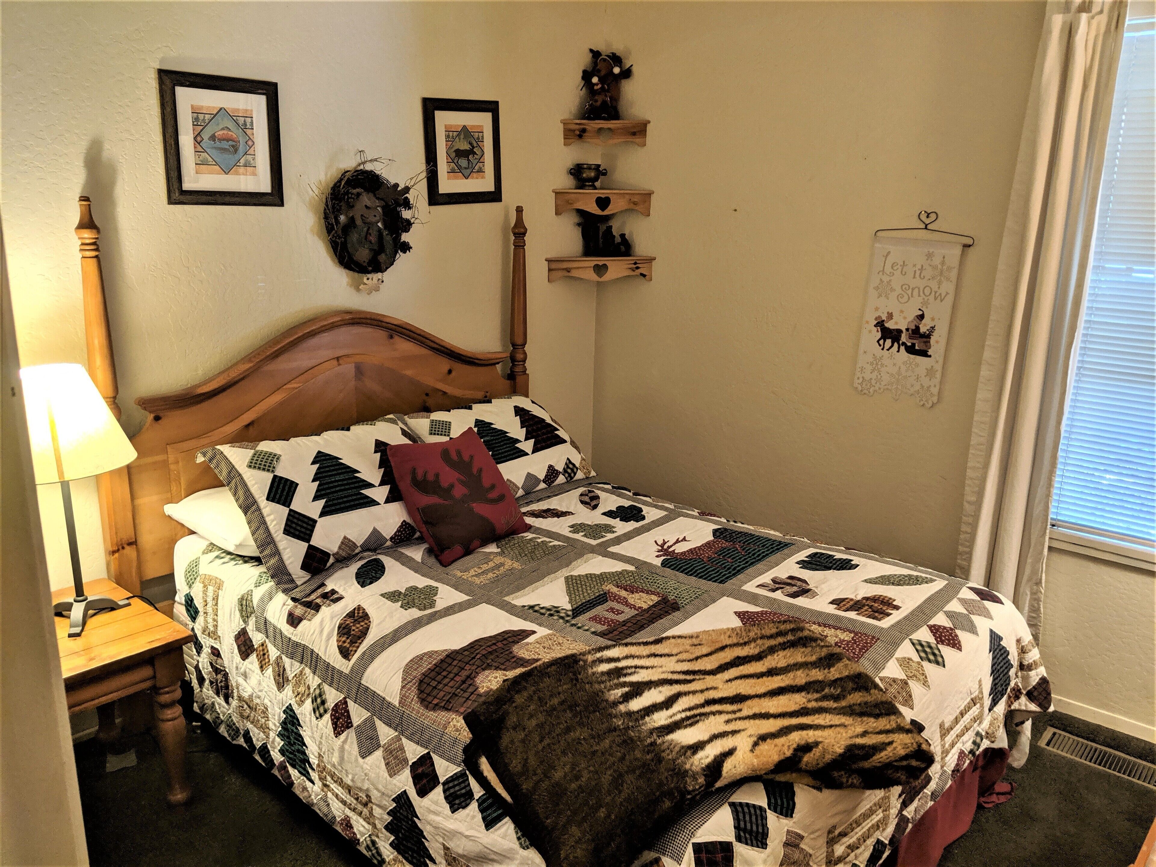 Ein Schlafzimmer mit einem hölzernen Bett, einer Decke mit Tiermotiven, einer Lampe und Wanddekorationen, darunter gerahmte Bilder und ein Schild.