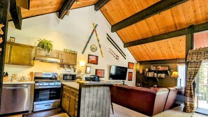 Une cuisine avec un plafond en bois, une cuisinière encastrée, un four à micro-ondes et un téléviseur. On y trouve également un coin bar avec un banc rembourré et une plante posée sur le comptoir.