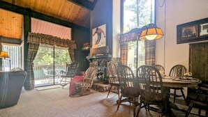 Un coin repas rustique avec des chaises et une table en bois, une cheminée et de grandes fenêtres ornées de rideaux.