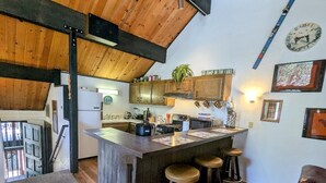 Une cuisine avec des meubles en bois, un coin bar avec des tabourets, une horloge et un panneau sur lequel on peut lire : « ALLEZ, PLONGEZ DANS LE LAC ! »