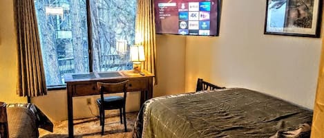 Een slaapkamer met een bed, een bureau en een tv aan de muur.
