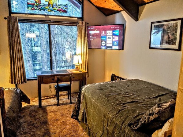 A cozy room with a bed, a desk, and a TV mounted on the wall.